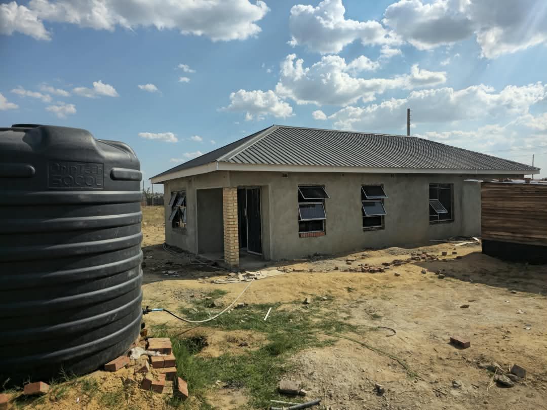 The plastered three-bedroom house in Bulawayo with its roof on and a water tank beside it