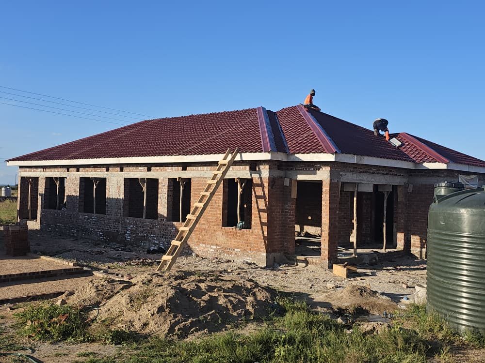 Champs roofers fixing red roof sheets on a large brick house