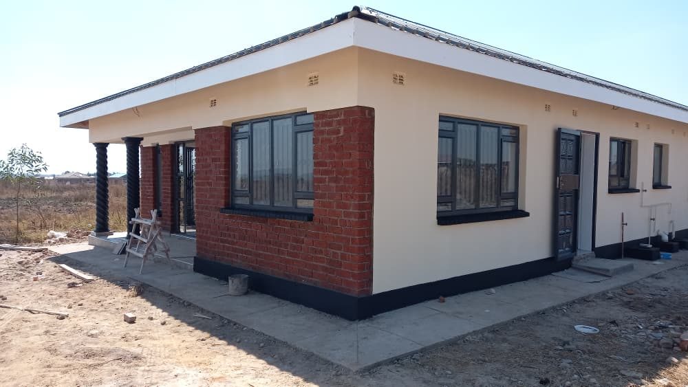 A completed cream house with a black plinth, dark windows and a face-brick entrance