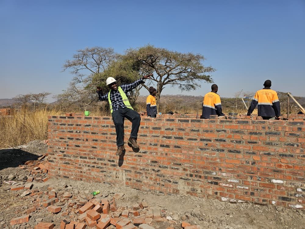 Builders on a brick wall rising from the foundations