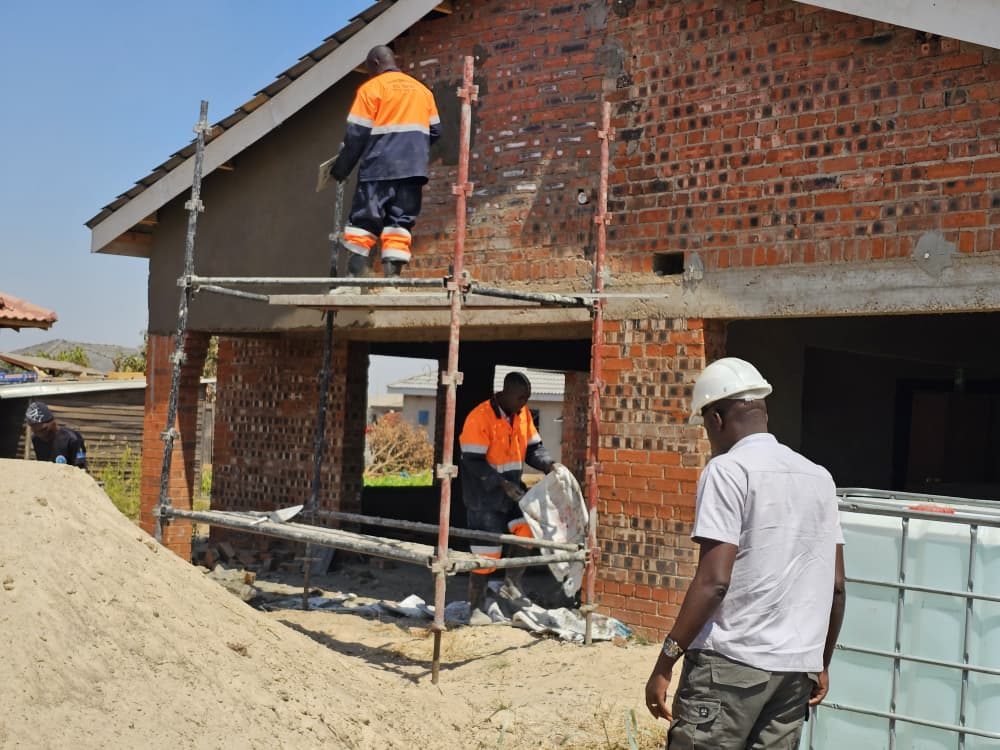 Builders on scaffolding plastering a house with a tiled roof